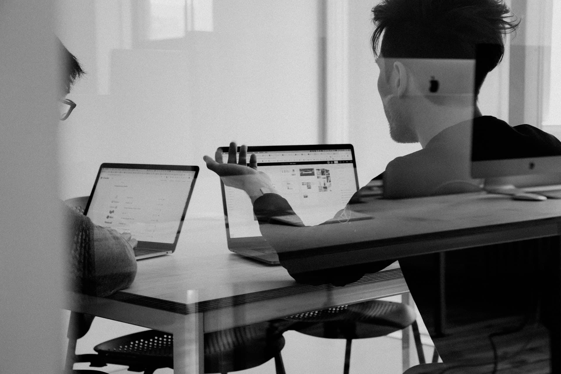 Dos colaboradores revisando informacion en sus laptops en una oficina